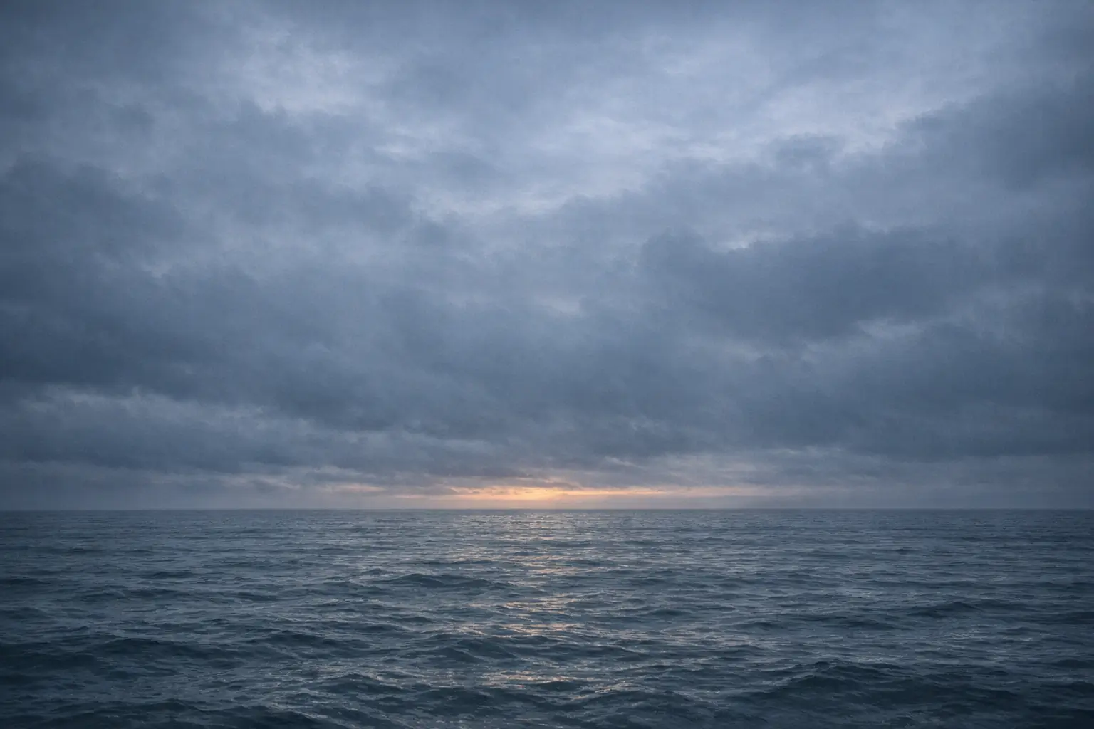 Calm ocean waters meeting the horizon under a brooding overcast sky at dawn